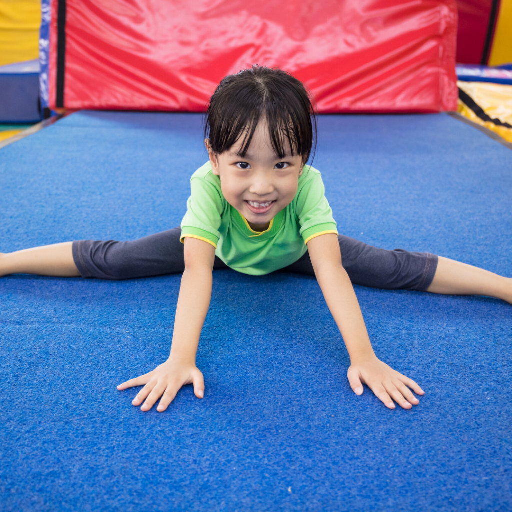 A child smiling at the camera while doing the splits