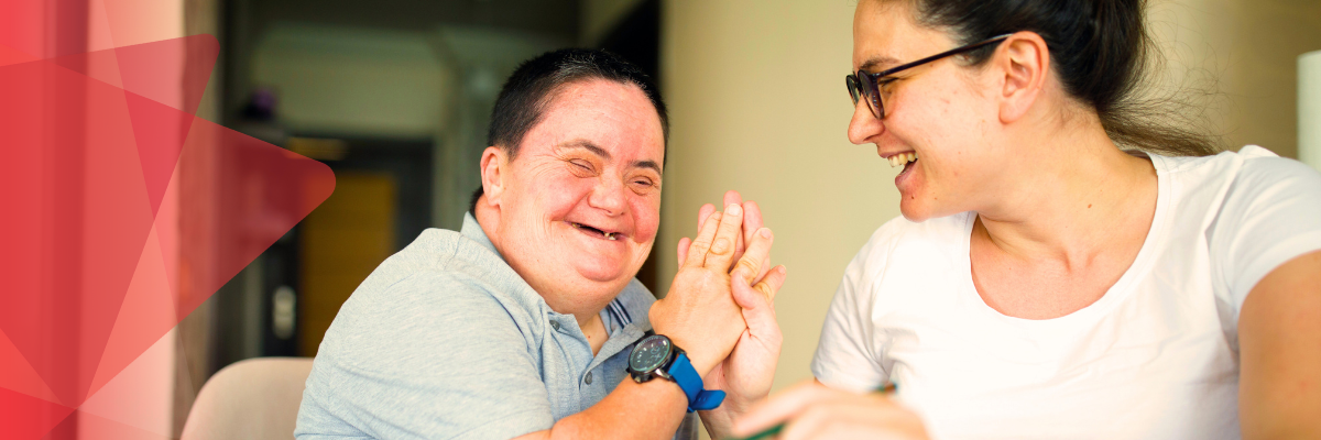 A Y support worker laughign and high-fiving her male client in his home.