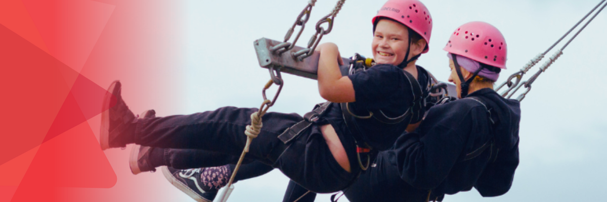 Camper and Y Support worker smiling on a giant swing at camp